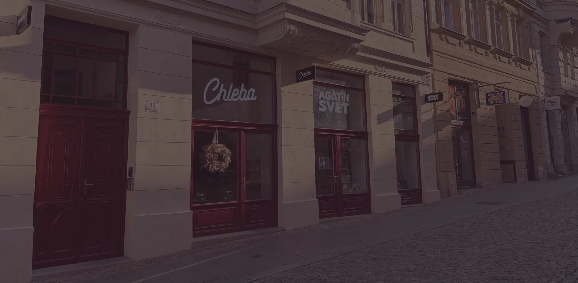 Obnovený parter domu Starobrněnská 13 s dřevěnými výkladci a pekařstvím Chleba Brno ve večerním světle, červen 2026