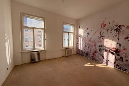 Pokoj se dvěma okny do ulice a růžovou květinovou tapetou, podlaha zatím holá, srpen 2025
