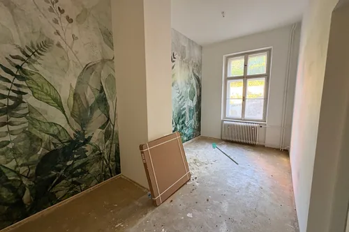 Pokoj se zelenou tapetou s listy po obou stranách pilíře, podlaha zatím holá, srpen 2025