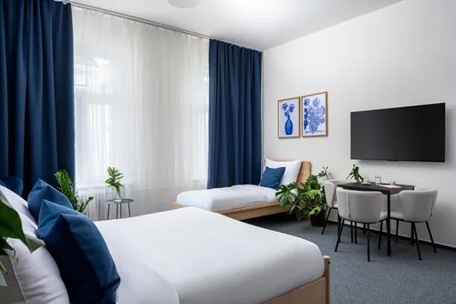 Hotelový pokoj s manželskou postelí, modrými závěsy a jídelním stolkem, hotel Botanica, říjen 2025