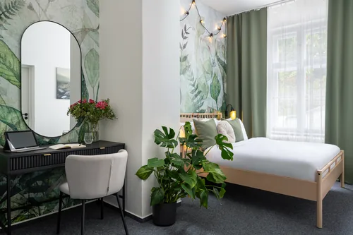 Pokoj s psacím stolem, oválným zrcadlem a postelí u okna, hotel Botanica, říjen 2025