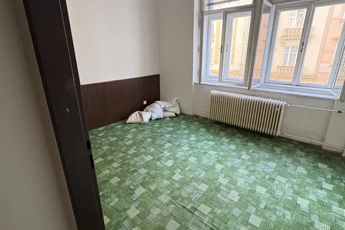 Pokoj dřívějšího ubytování se zeleným vzorovaným kobercem a sdruženým oknem, Hlinky 28a, srpen 2025