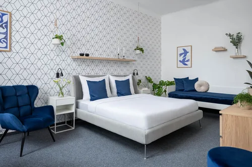 Hotelový pokoj v modrobílé kombinaci s manželskou postelí a sametovým křeslem, hotel Riverside, červenec 2025