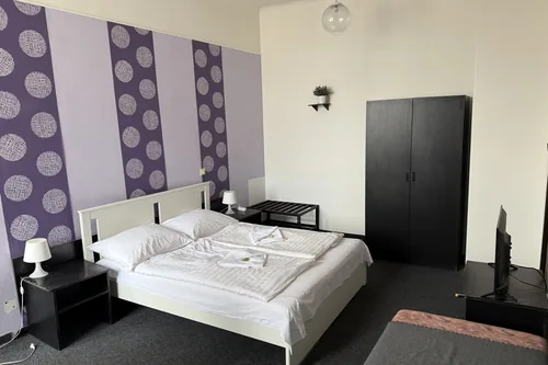 Pokoj původního hotelu s fialovou tapetou, manželskou postelí a přistýlkou, březen 2025
