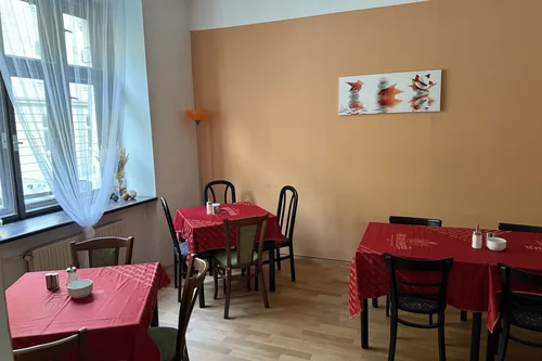 Původní snídaňová místnost hotelu se stoly s červenými ubrusy a oranžovou stěnou, březen 2025