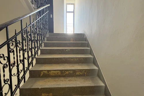 Schodiště po stržení starého koberce, zachované kované zábradlí, květen 2025